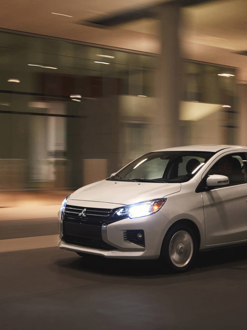 A white 2024 Mitsubishi Mirage G4 Sedan driving fast through the city