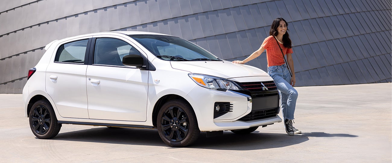 Mujer apoyada en un Mitsubishi Mirage 2023 blanco estacionado hatchback
