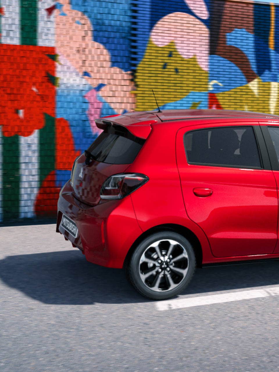 A red 2024 Mitsubishi Mirage Compact Hatchback parked in front of a colorful mural