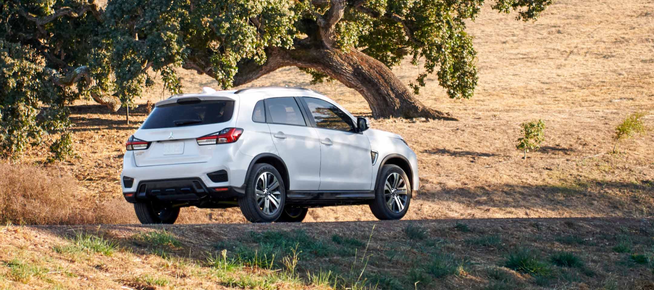 Rear and side view of a white 2022 Mitsubishi Outlander Sport driving in a rural road