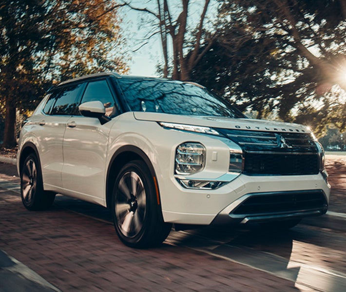 2026 Mitsubishi Outlander SUV driving on a road lined with trees showing off the Speed Limit Assist feature