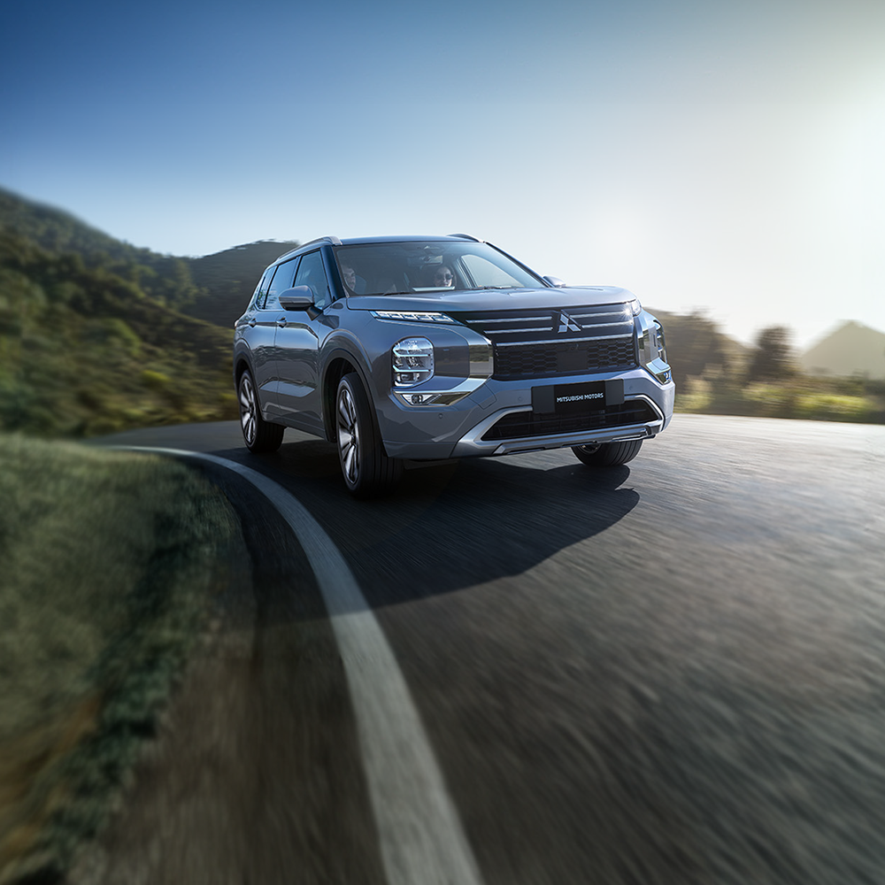 View from inside of open 2026 Mitsubishi Outlander SUV driver door with a person sitting in driver seat and a person leaning against open door.