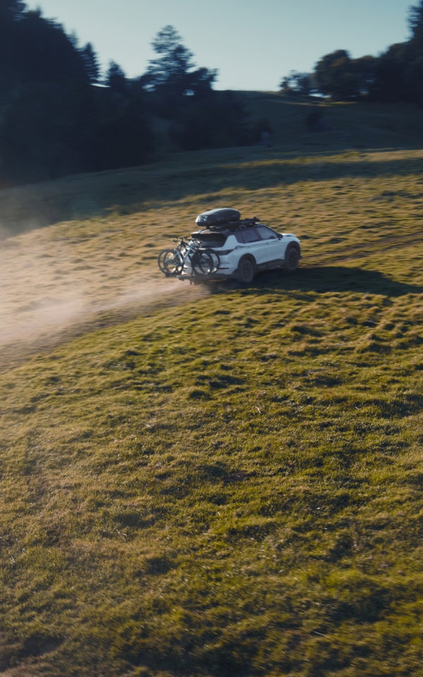 A white 2025 Mitsubishi Outlander Trail Edition SUV driving through a field