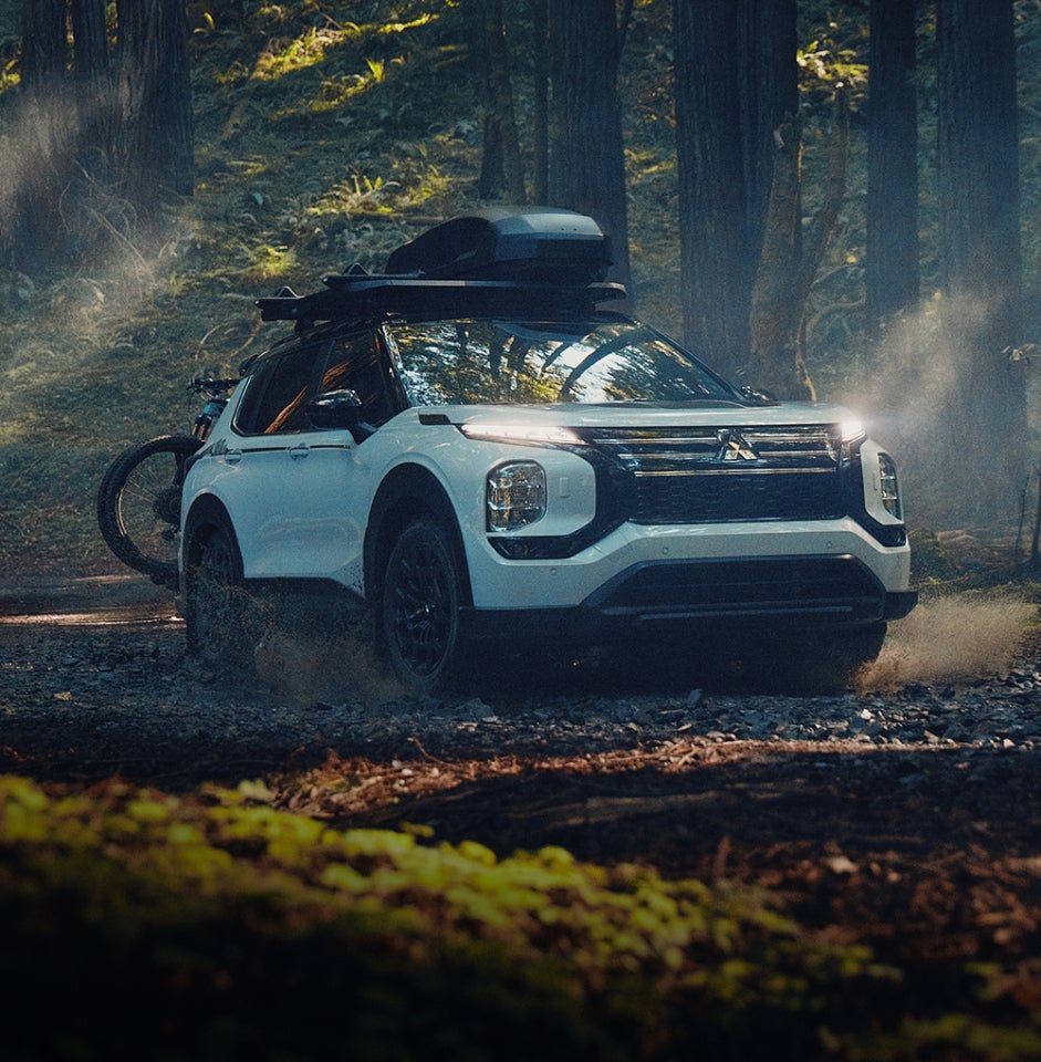 A white 2025 Mitsubishi Outlander Trail Edition SUV in the forest